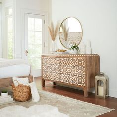 a room with a white rug and a wooden dresser in the corner, next to a mirror