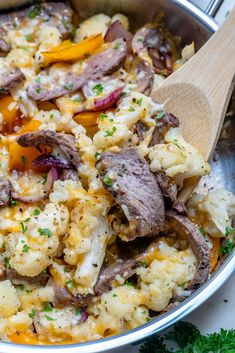 a pot filled with meat and vegetables on top of a table next to a wooden spoon