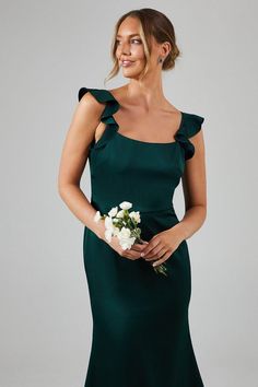 a woman in a long green dress holding a white flower and posing for the camera