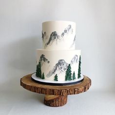 a three tiered cake decorated with mountains and pine trees on a wooden platter