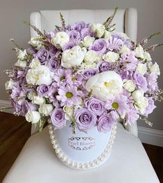 purple and white flowers are in a blue vase on a chair with pearls around it