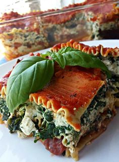 lasagna casserole with spinach and tomato sauce on white plate next to glass dish