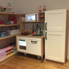 a play kitchen with white cabinets and wooden floors