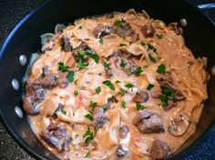 a skillet filled with pasta and meat covered in mushroom sauce, garnished with parsley