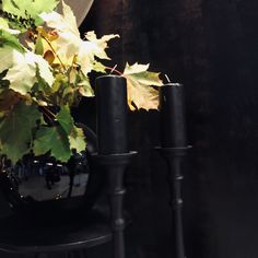 two black candles sitting on top of a table next to a vase filled with leaves