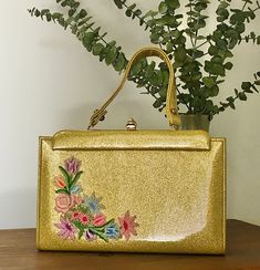 "1950s Faye Mell Designs Miami Gold Glitter Vinyl Top Handle Handbag, Vintage Floral Purse, Mid Century Accessory Glamorous 1950s Faye Mell Designs Miami gold glitter top handle handbag that features: Gold glitter fabric that's lightly padded exterior with a clear plastic covering. Single handle strap handle. Gold tone metal frame, hardware and chic clasp closure that works well and closes tightly. Raised multi colored floral appliqué on one side. Opens to a gold faille lining with one interior side metal zippered pocket and one interior side open slip pocket. Attached Exclusively Faye Mell Design Fleurette, Inc. Miami Fla. label. No International shipping on this item. Nearest mint condition *the exterior shows no signs of use.  It is immaculate.  The lining is immaculate.  The hardware s Mid Century Accessories, Design Miami, Glitter Top, Handbag Vintage, Floral Purse, Top Handle Bags, Top Handle Handbags, Vintage Purses, Miami Design