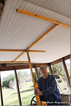 an older man holding a yellow object in his hand while standing next to a window