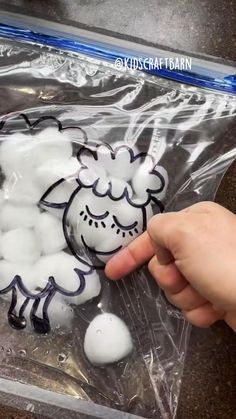 a hand is pointing at some white balls in a plastic bag that have been filled with black and white sheep