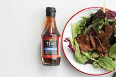 a white plate topped with meat and salad next to a bottle of hot sauce on a table