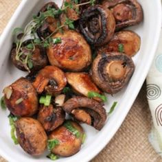 a white bowl filled with mushrooms and greens on top of a tablecloth next to a napkin