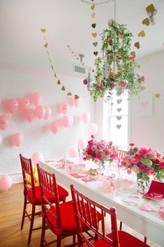 a long table with red chairs and pink balloons hanging from it's ceiling in a white room