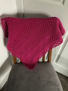 a pink knitted blanket sitting on top of a chair next to a white door