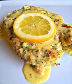 a white plate topped with chicken covered in gravy next to a lemon wedge