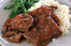 a white plate topped with meat and gravy next to green beans