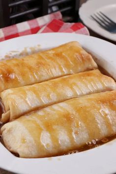 two burritos sitting on top of a white plate next to a red and white checkered table cloth