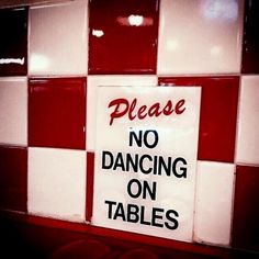 a sign that says please no dancing on tables in front of red and white tiles