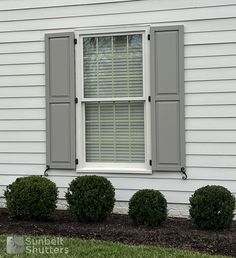 a white house with gray shutters on the windows and bushes in front of it