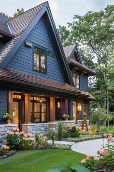 a blue house with lots of windows and flowers in the front yard, surrounded by greenery