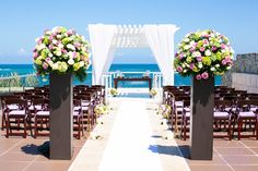 an outdoor ceremony set up with flowers and white draping on the beach side