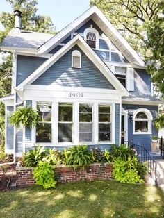 a blue house with lots of windows and plants in the front yard on a sunny day