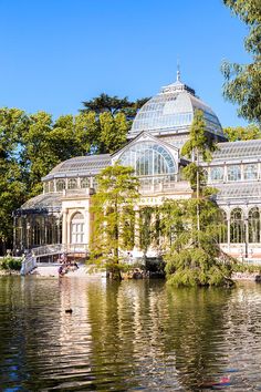 a large building sitting on top of a lake next to a lush green forest filled with trees