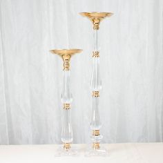 two clear and gold candlesticks sitting on a table next to a white curtain