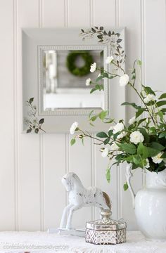 a white vase with flowers on a table next to a mirror and a small figurine