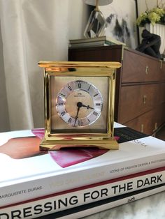 a gold clock sitting on top of a stack of books next to a lamp and dresser