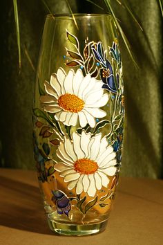 a glass with flowers painted on it sitting on a table