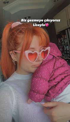 a woman with red hair and heart shaped sunglasses holding a small child in her arms