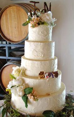 a white wedding cake with flowers and vines on top sits in front of wine barrels