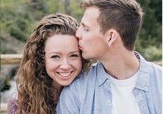 a man and woman kissing each other with trees in the background