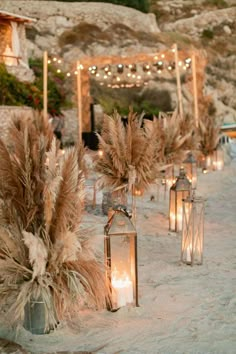 an outdoor setting with candles and flowers in vases on the sand, surrounded by lights