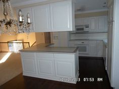 an empty kitchen with white cabinets and chandelier