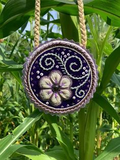 a purple glass ornament hanging from a rope in front of some green plants