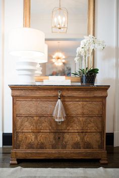 a dresser with a lamp and flowers on top