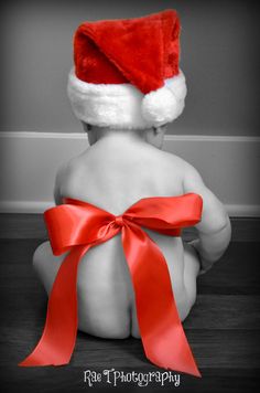 a black and white photo of a baby wearing a santa hat with a red ribbon