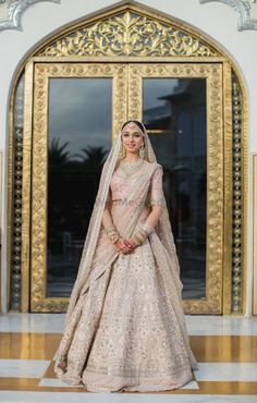 a woman in a white and gold bridal gown posing for the camera with her hands on her hips