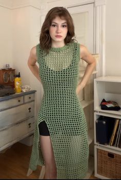 a woman standing in front of a dresser wearing a green crochet dress with high slits