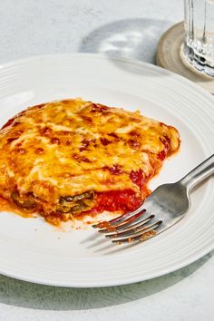 a white plate topped with lasagna next to a fork and glass of water