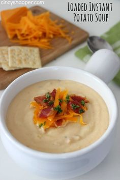 a bowl of loaded instant potato soup next to crackers and cheese on a cutting board