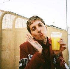 a man with tattoos holding a glass of orange juice