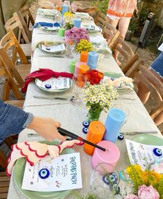 a long table is set with flowers and cards for someone to place their plates on