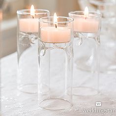 candles are lit in clear glass vases on a table