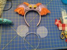 a mickey mouse ears head on top of a cutting board with scissors and other crafting supplies