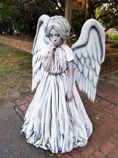 a statue of an angel with white hair and blue eyes standing on a brick walkway