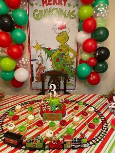 a table topped with lots of cupcakes and cake next to balloons in the shape of christmas trees