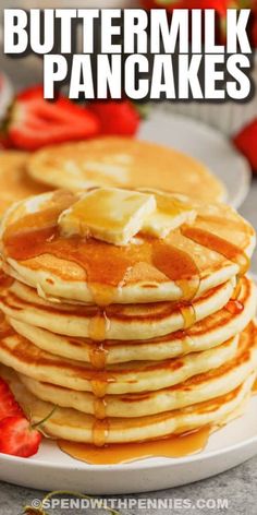 stack of buttermilk pancakes on a plate with syrup and strawberries in the background