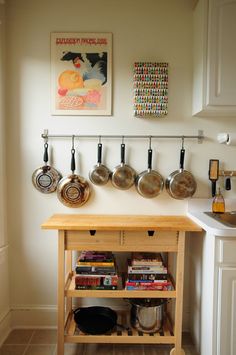 pots and pans are hanging on the wall above a wooden table in a kitchen