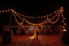 a bride and groom standing under string lights